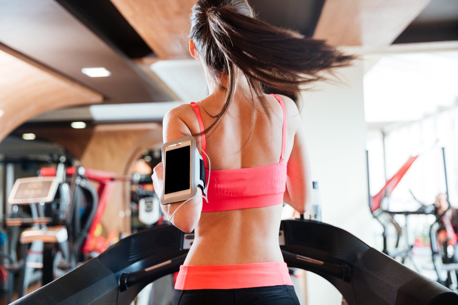 woman running on treadmill with phone attached to arm