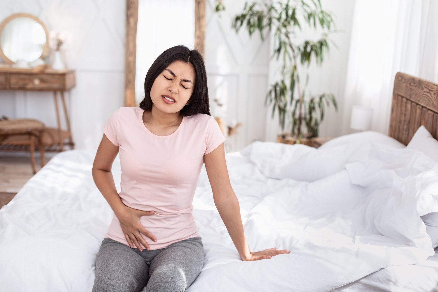 Woman sitting on bed holding belly in pain