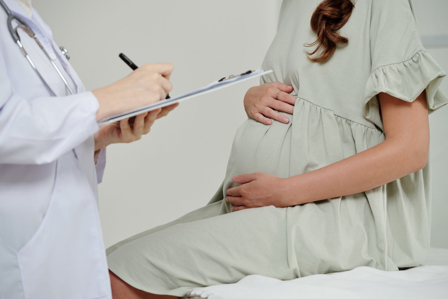 Woman holding pregnant belly while talking to doctor